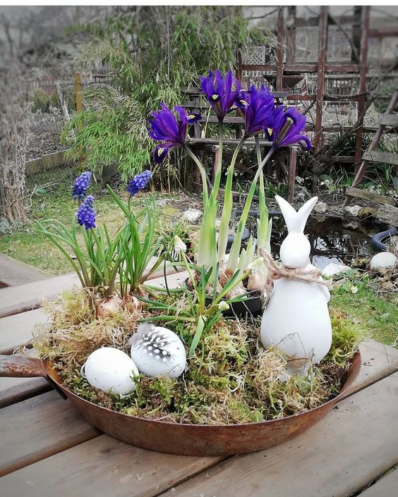 A rustic Easter decoration made from an old pan, moss, artificial eggs and feathers, a bunny and fresh flower bulbs is ideal for outdoor use