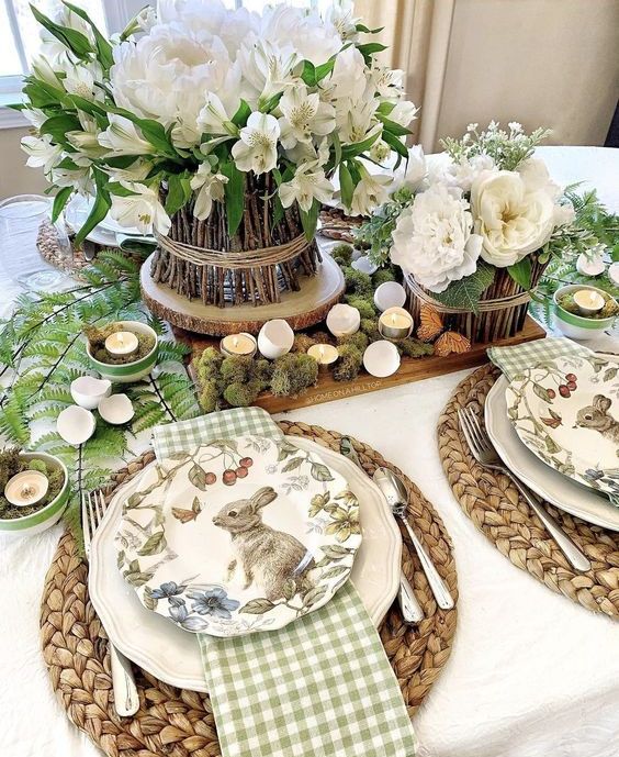 a rustic Easter tablescape with a tray of moss, eggshell candles, white flowers and greenery, woven placemats and printed plates, and checkered napkins