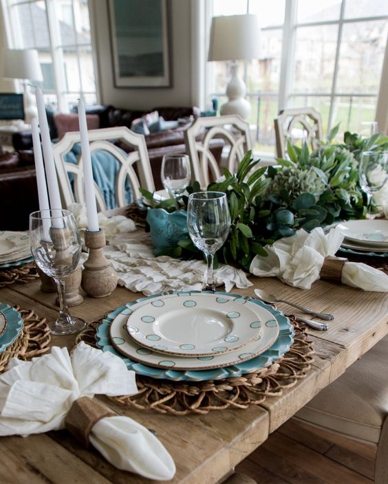 a rustic Easter tablescape with woven placemats, a green centerpiece, wooden candle holders with candles, neutral napkins and printed plates
