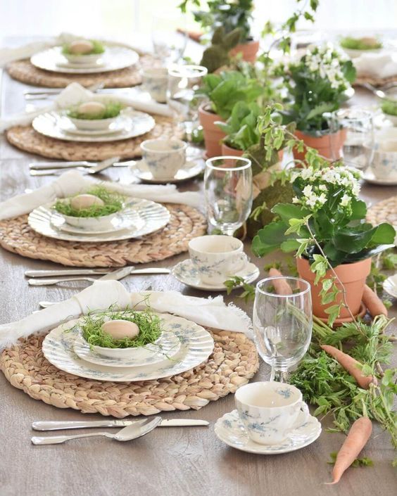 a rustic Easter tablescape with woven placemats, printed china, potted flowers and greenery, and nests of eggs
