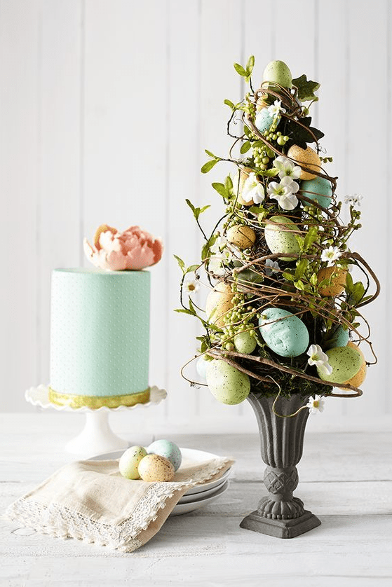 an Easter flower arrangement in the shape of a tree - with vines, green plants, flowers and pastel-colored eggs