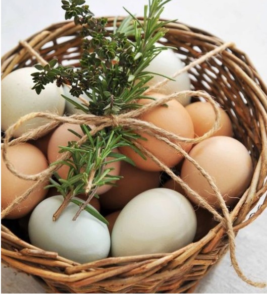 A simple and cute rustic Easter decoration made from a basket of eggs in natural and pastel colors, twine and greenery is a cool idea for a mantel or console table